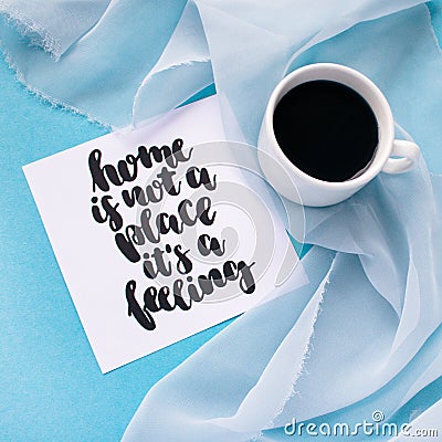 Mug of coffee on pale blue pastel chiffon cloth on a blue background. Card with handwritten inspirational quote Home is not a plac Stock Photo