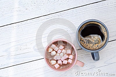 Mug of hot chocolate with small marshmallows next to a mug of black coffee isolated on white painted wood from above. Space for Stock Photo