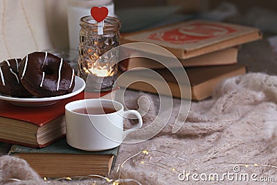 Mug with tea, books, donuts and woolen plaid winter blanket on vintage wooden table, autumn winter seasonal background, concept of Stock Photo