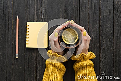 Mug of tea with lemon in a female hand, pencil and notepad. Wood Stock Photo