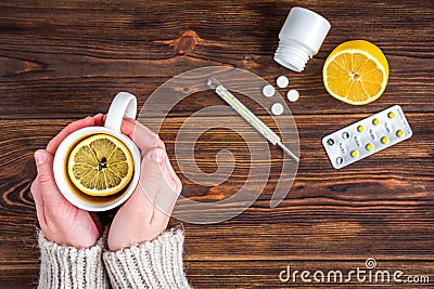 Mug of tea with lemon in female hands. Lemon, thermometer and pills on wooden background. Cold treatment. Flu season Stock Photo