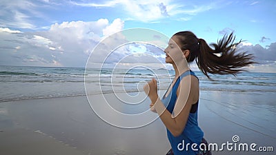 Mujer activa sana en el funcionamiento superior del azul en la playa cerca del mar en puesta del sol almacen de metraje de vídeo Mujer activa sana en el funcionamiento superior del azul en la playa cerca del mar en puesta del sol almacen de metraje de vídeo