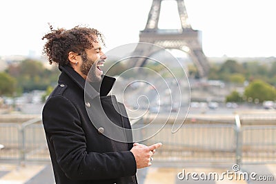 Mulatto laughing guy around Eiffel Tower with smartphone Stock Photo