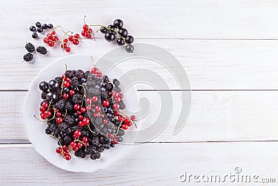 Mulberry berries, blackberries and currants on a white plate on background wooden table. The flat composition Stock Photo