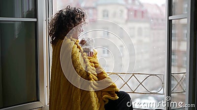 Mulher de cabelo encaracolado envolveu-se num cobertor amarelo com um gato na janela e olhando a queda de neve na rua Mulher de cabelo encaracolado envolveu-se num cobertor amarelo com um gato na janela e olhando a queda de neve na rua