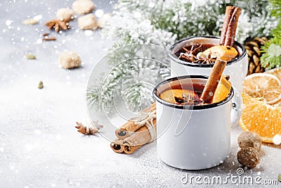 Mulled wine in white metal mugs with cinnamon, spices and orange with fir tree and christmas lights - traditional drink on winter Stock Photo