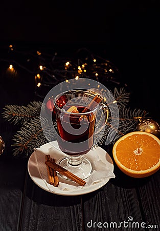 Mulled wine on white plate on black wooden table, cinnamon sticks and orange, christmas tree and lights Stock Photo