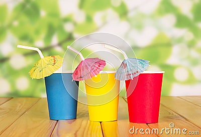 Multi-colored disposable paper cups and straws on abstract green. Stock Photo