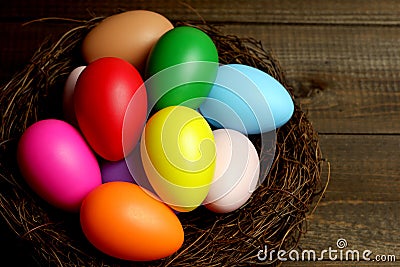 Multi colored easter eggs in birds nest on dark wooden planks table top closeup view selective focus. Easter holiday banner, card Stock Photo