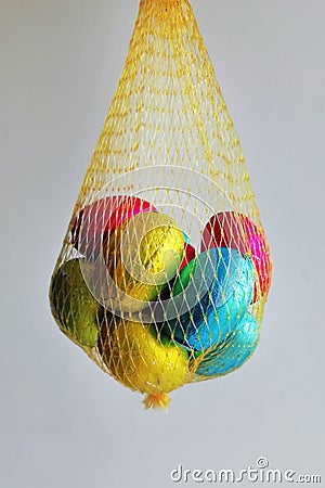 Multi colored eggs wrapped in foil folded into a yellow mesh. Stock Photo