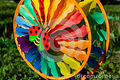 Multi colored round pinwheel in motion, in sunny garden. Big round rainbow pinwheel in motion. Stock Photo