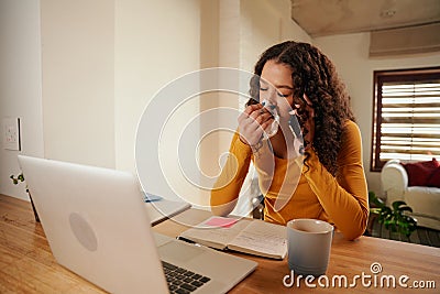 Multi-cultural Young professional blowing nose while taking business call. Remote working female sick at home Stock Photo