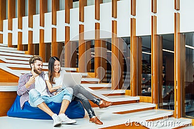 Multi-ethnic college student couple celebrate together with laptop on stairs in university campus or modern office Stock Photo