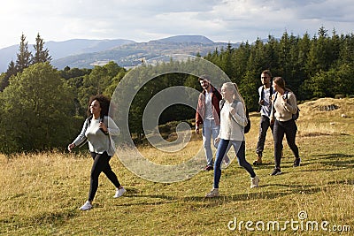 A multi ethnic group of five young adult friends smile while walking on a rural path during a mountain hike, side view Stock Photo