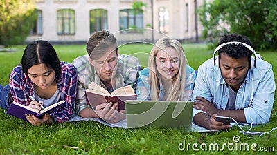 Multi-ethnic men and women doing homework on grass on campus, higher education Stock Photo