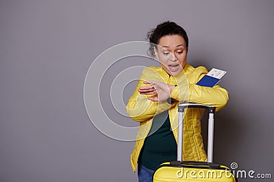 Multi-ethnic woman in yellow jacket, checks time on her wrist watch, feeling anxious being unpunctual at her flight Stock Photo