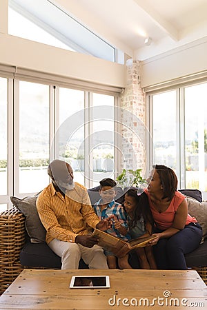 Multi-generation family reading a story book in living room Stock Photo