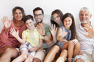 Multi Generation Family Sitting Against Wall And Waving Stock Photo