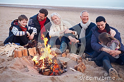 Multi Generation Family Sitting By Fire On Winter Beach Stock Photo