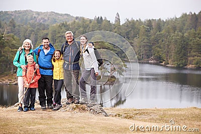 Multi generation family stand embracing by a lake, smiling to camera, front view, Lake District, UK Stock Photo