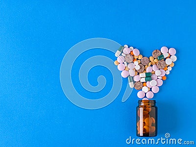 Multicolored heart-shaped pills pour out of a glass brown bubble on a blue background Stock Photo