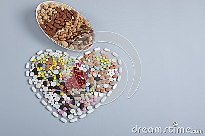 Multicolored pills in shape of heart and different nuts in bowl on gray background. Concept of traditional medicine Stock Photo