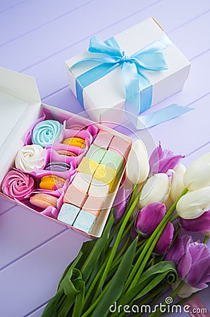 Multicolored set of different sweet marshmallow and macaroons in gift box and bouquet of tender tulips Stock Photo