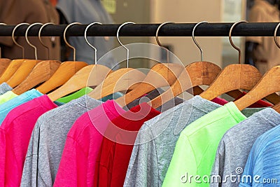 Multicolored shirts and sweatshirts hang on wooden hangers close up Stock Photo
