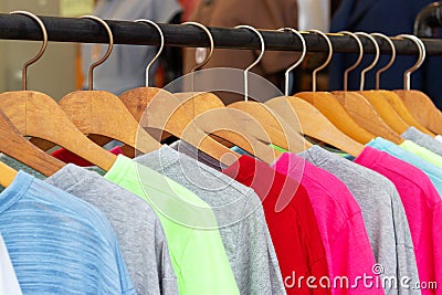 Multicolored shirts and sweatshirts hang on wooden hangers close-up side view Stock Photo