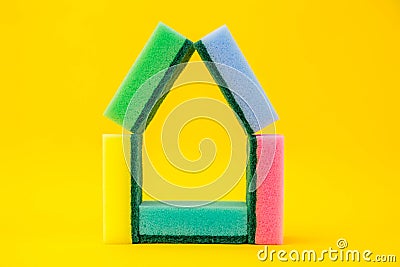 Multicolored sponges for cleaning folded in the shape of a house on a yellow background. Space for text Stock Photo