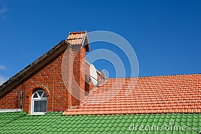 Multicolored tiled roofs of houses against the blue sky with clouds Background Attics Orange and green color. Stock Photo