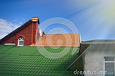 Multicolored tiled roofs of houses against the blue sky with clouds Background Attics Orange and green color Sun rays Stock Photo