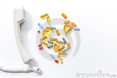 Multicoloured pills with phone handset on white background top view call doctor Stock Photo