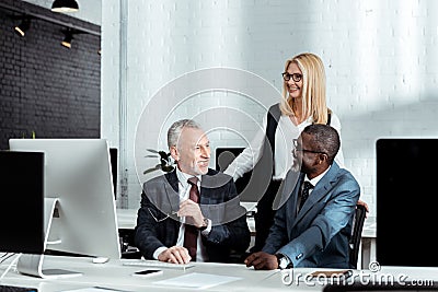Multicultural businessmen smiling near attractive woman Stock Photo