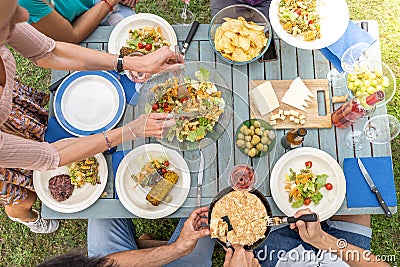 Multicultural family sitting at wooden table having dinner. They have plates full of food and glasses with drinks. Stock Photo