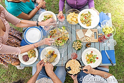 Multicultural friends sitting at wooden table. Friends having dinner. They have plates full of food and glasses with Stock Photo