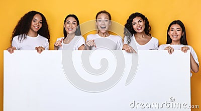 Multicultural Ladies Holding Empty Paper Board Over Yellow Background, Mockup Stock Photo