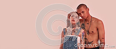 Darkskinned topless guy with tattoos standing behind a white pierced tattoed adult girl, hugging her from a back Stock Photo