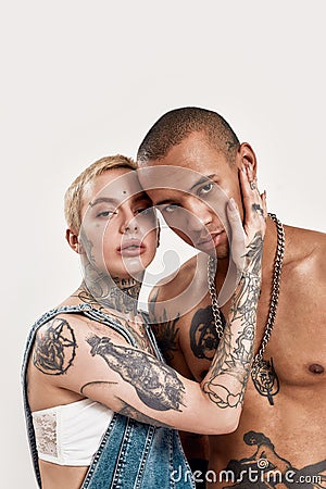 Multicultural relationship. A white pierced woman with tattoos touching a dark-skinned tattooed topless guy standing Stock Photo