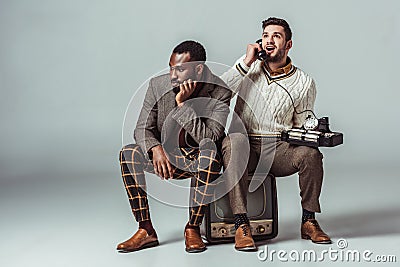 multicultural retro styled friends sitting on old tv and talking Stock Photo