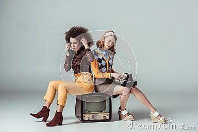 multicultural retro styled girls sitting on old tv and talking Stock Photo