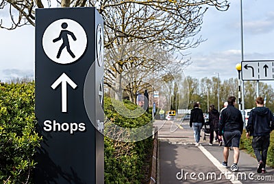 Multidirectional wayfinding sign with arrow and person walking icon pointing towards shops. Editorial Stock Photo