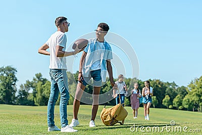 multiethnic boys playing with rugby ball while classmates walking behind Stock Photo