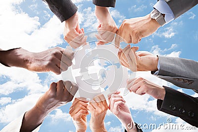 Multiethnic business people assembling jigsaw puzzle against sky Stock Photo