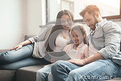 Multiethnic family using digital tablet while sitting on sofa at home Stock Photo