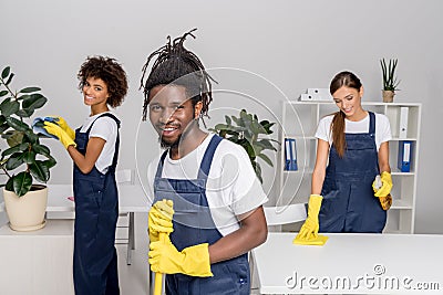 multiethnic group of professional cleaners in rubber gloves smiling at camera while Stock Photo