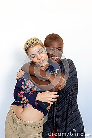Photo of multiethnic joyful ladies embrace and enjoy togetherness while looking at camera against background Stock Photo