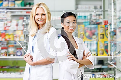 multiethnic pharmacists in white coats standing with crossed arms and smiling at camera Stock Photo