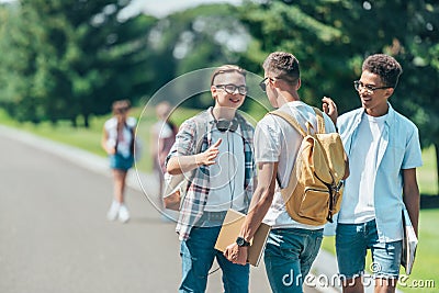 multiethnic teenage boys with books and backpacks talking and smiling each other Stock Photo