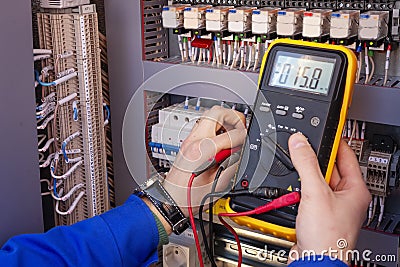 Multimeter in hands of electrician engineer in electrical cabinet. Maintenance of electric system Stock Photo